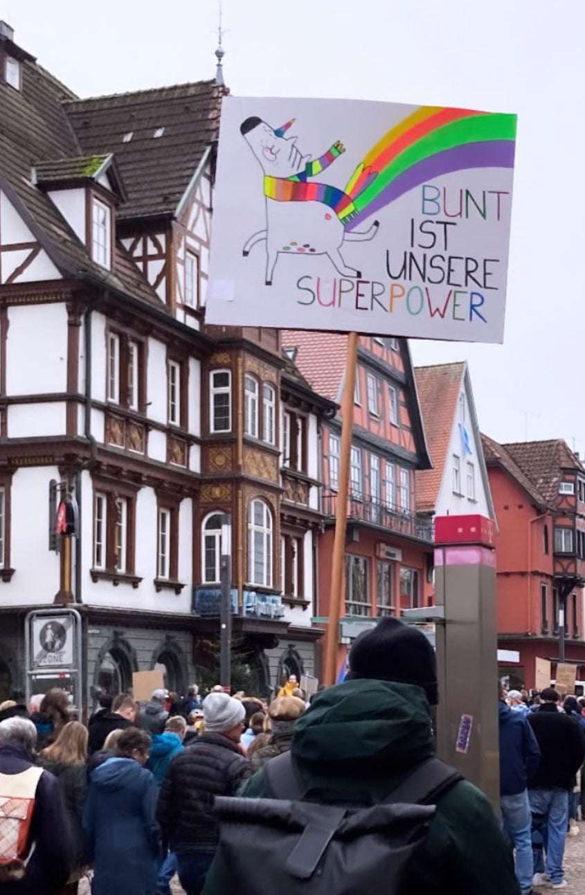 Demoplakat gegen rechts mit Schriftzug bunt ist unsere superpower und einem Einhorn von Halfbird das einen Regenbogen bunten Schal trägt