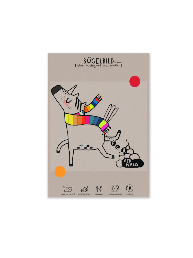 Produktansicht Buegelbild randlos FCK NZS Einhorn aufgeklebt auf Anleitungskarte, ein Einhorn mit Regenbogenschal, das einen Haufen macht auf dem FCK AFD und Nazis steht