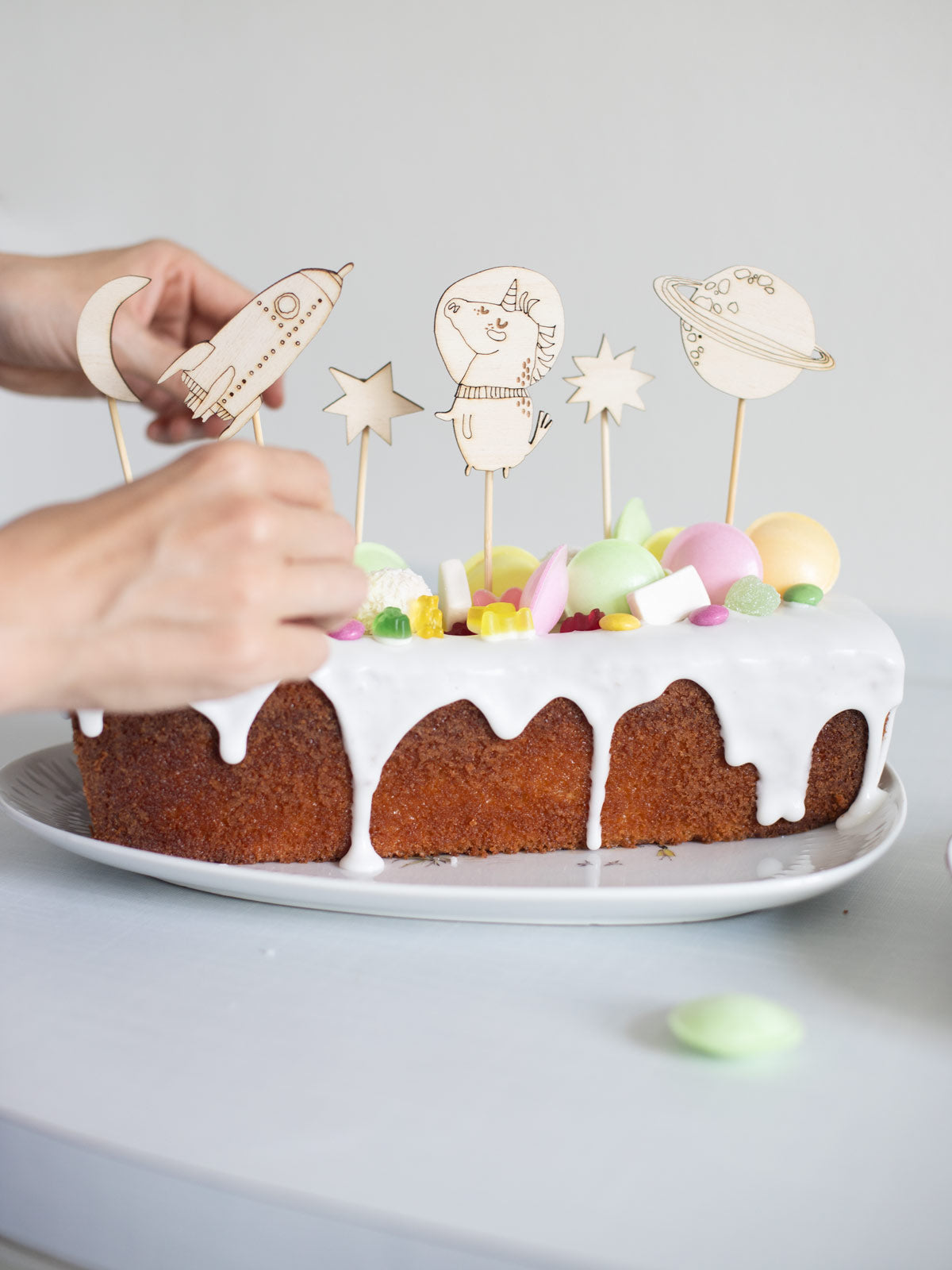 eine hand steckt einen weltraum caketopper auf einen verzierten Kuchen.