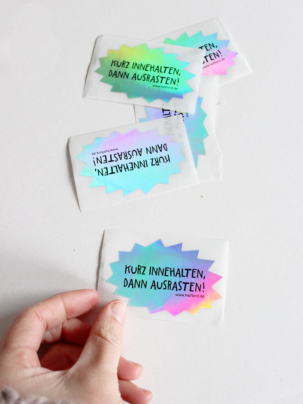 bild von mehreren hologramm stickern mit text kurz innehalten, dann ausrasten! von halfbird gehalten von hand