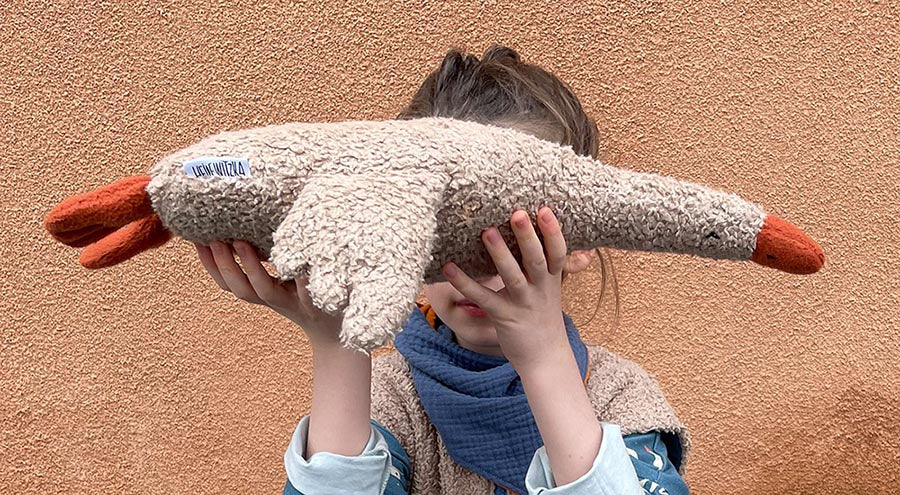 Kind hält eine genähte Gans Gerda vor ihren Kopf