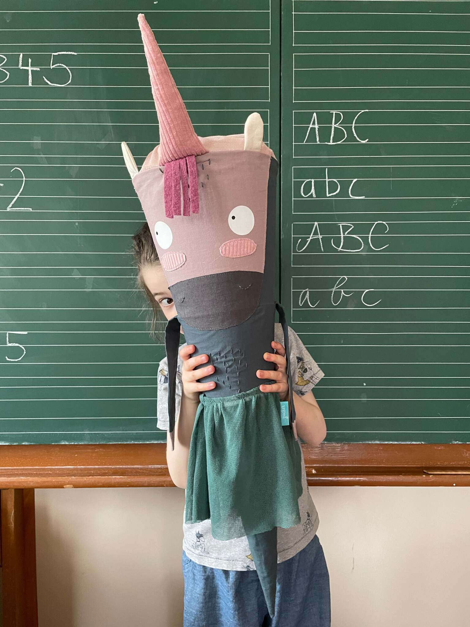 große Einhorn Schultüte ohne Glitzer, aber mit richtig viel Charme vor einer Schultafel. Für Mädchen oder Jungs zum Schulanfang. Sie trägt einen Tüllrock und hat Arme sowie Brusthaar