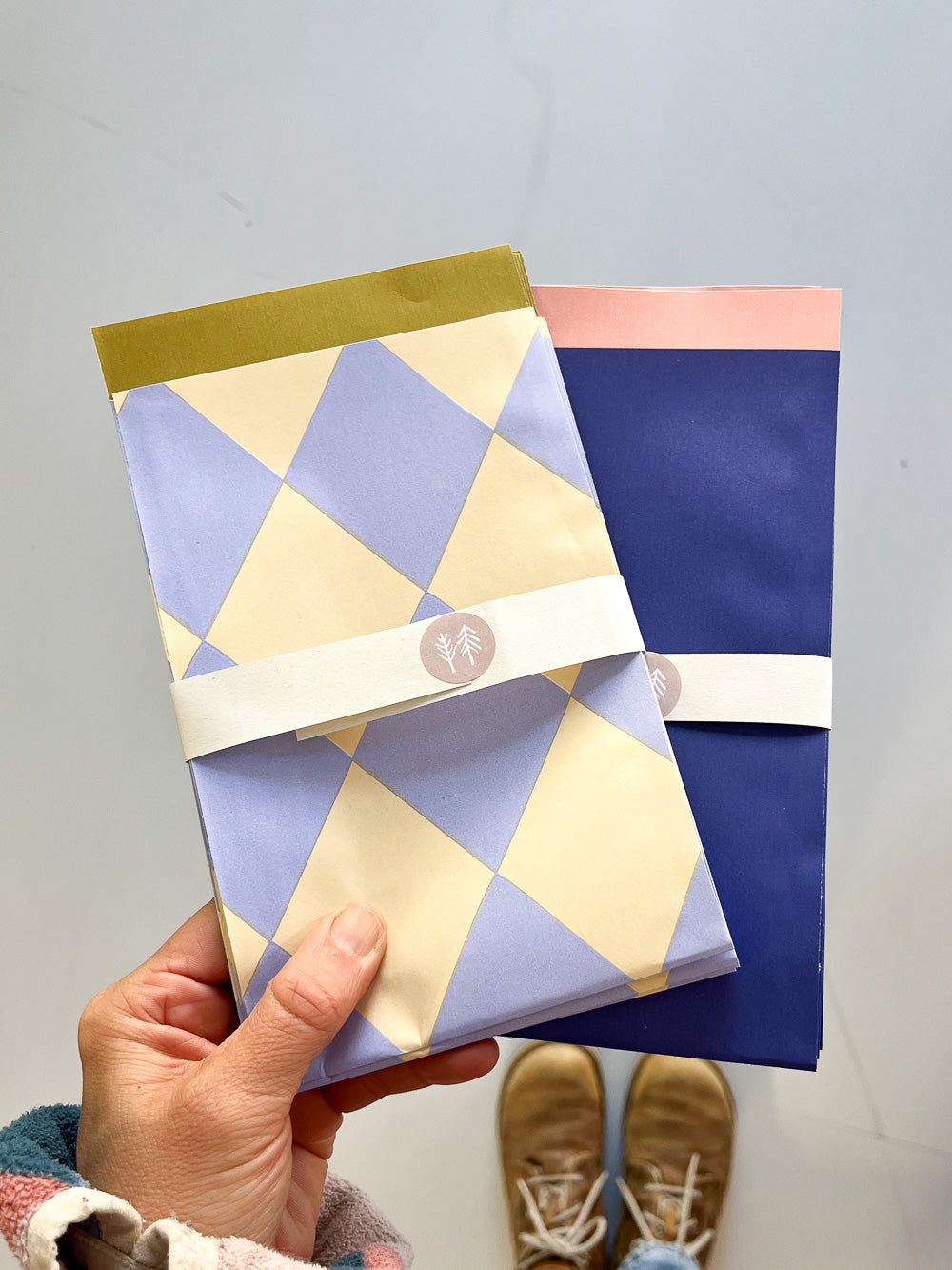 Hand mit Geschenktüten mit gelb-blauem Rautenmuster und dunkelblau-rosa Unimuster von Halfbird