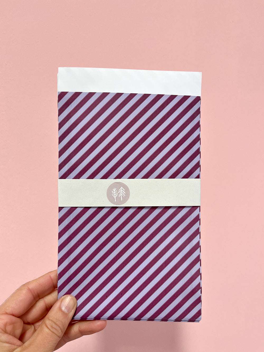Hand mit Geschenktüte mit lila-blauem Streifenmuster von Halfbird