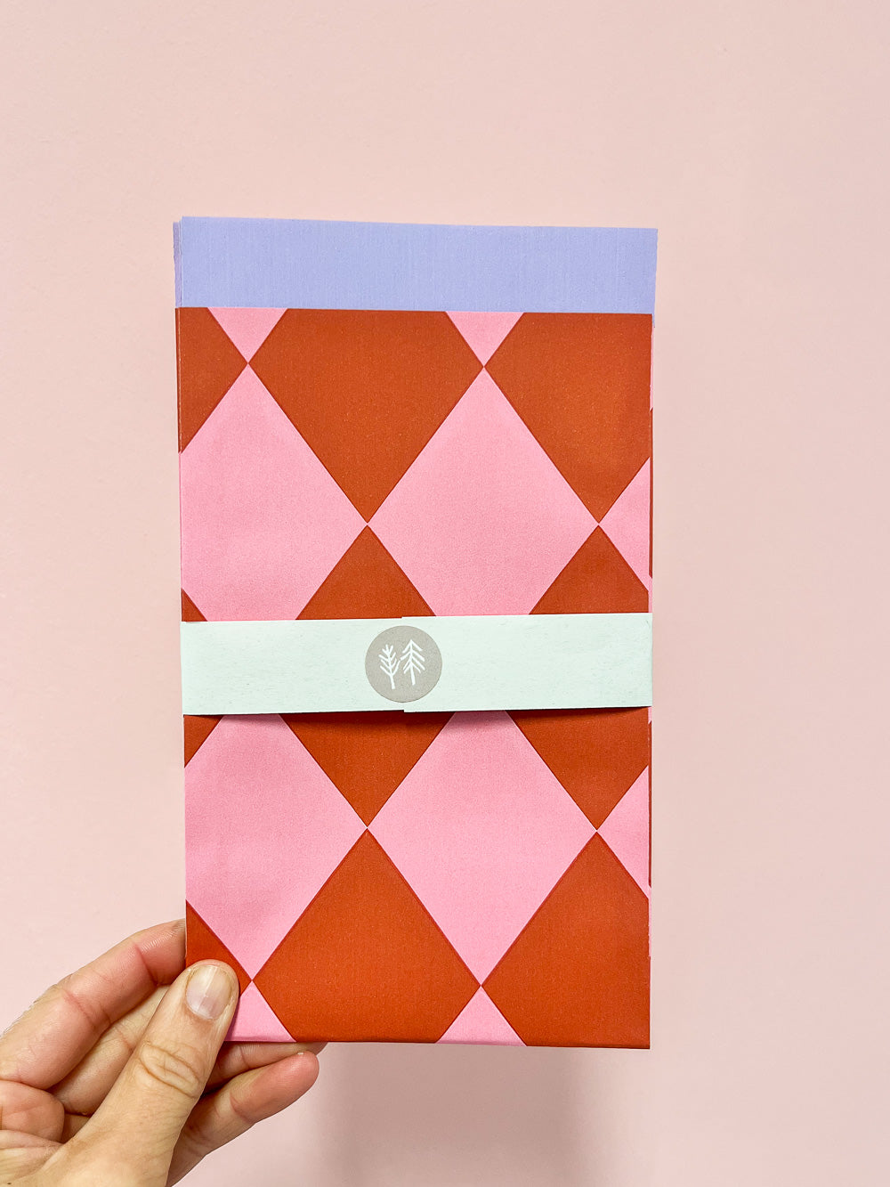 Hand mit Geschenktüte mit rosa-rotem Rautenmuster von Halfbird