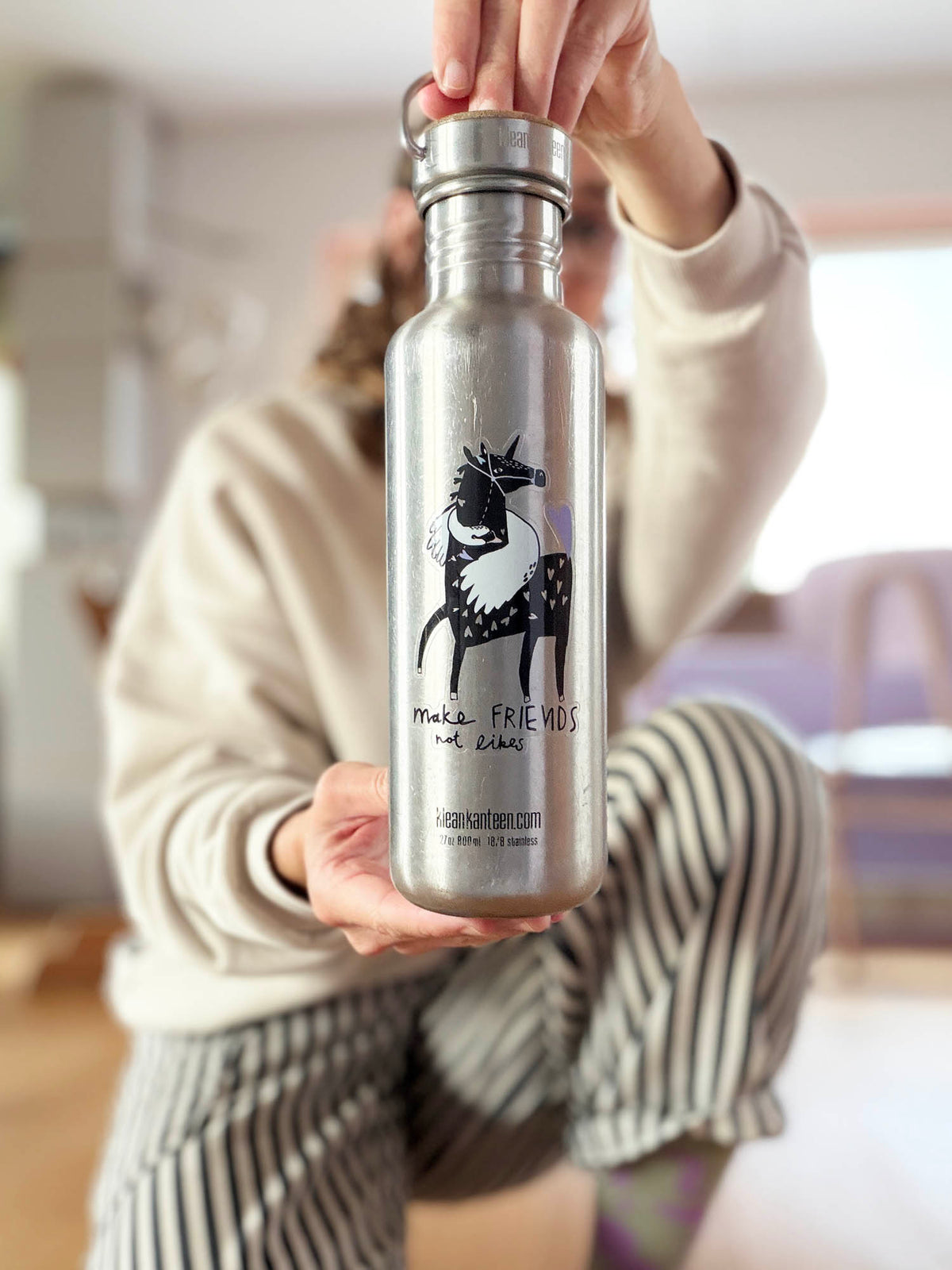 Mona hält Edelstahlflasche mit transparentem Vinylsticker Make Friends not Likes mit Pferd- und Schwanmotiv von Halfbird