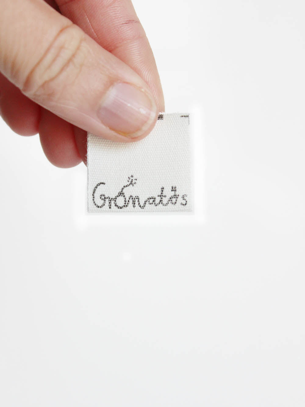in der Hand gehaltenes Nähetikett aus Biobaumwolle mit der Aufschrift Granatös in schwarz und einer kleinen Granate im a