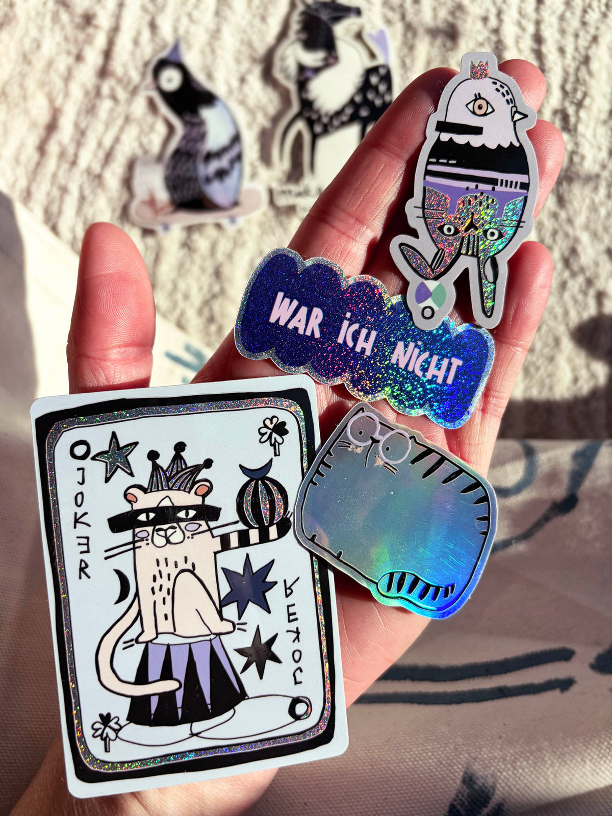 Hand mit verschiedenen Glitzer Stickern von Halfbird: die Joker Karte, Katze, War ich nicht und Taube und Hase