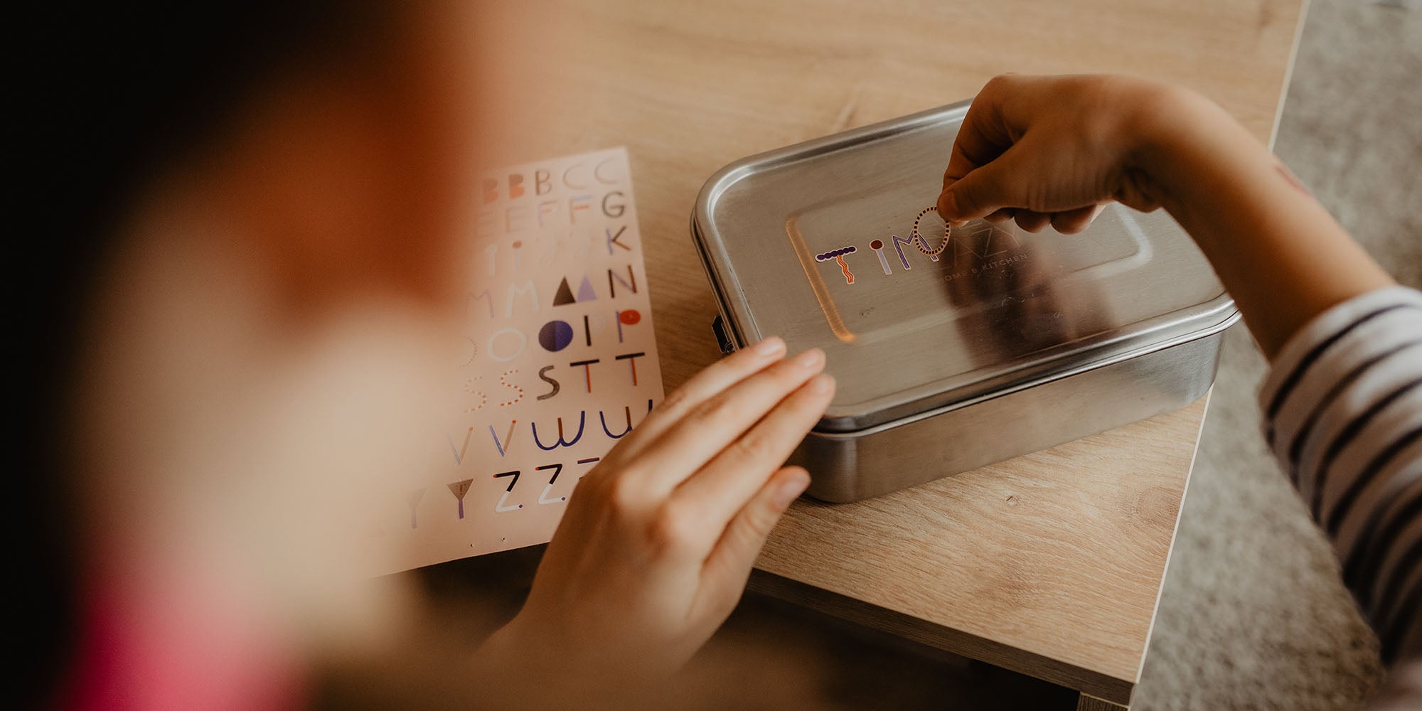 Kind klebt mit spülmaschinenfesten buchstaben aufklebern seinen Namen auf eine Brotdose aus Metall