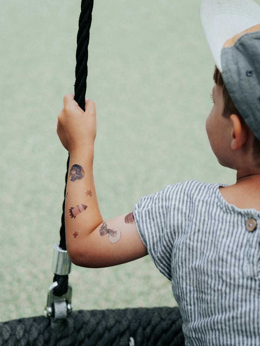 Kind schaukelt und hat einen tättowierten Arm mit Rakete, Planet, STerne und Schildkröte im Weltall als Astronaut