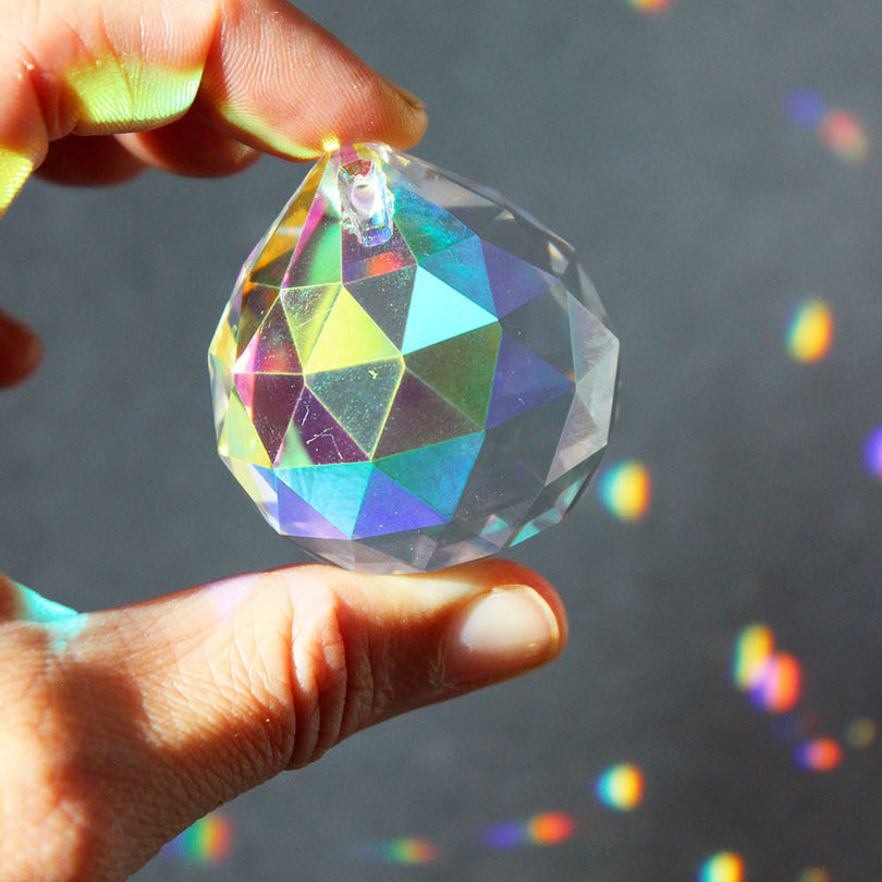 finger halten einen regenbogenkristall in perlmutt schimmernd und drum herum haben sich regenbogenpunkte gebildet