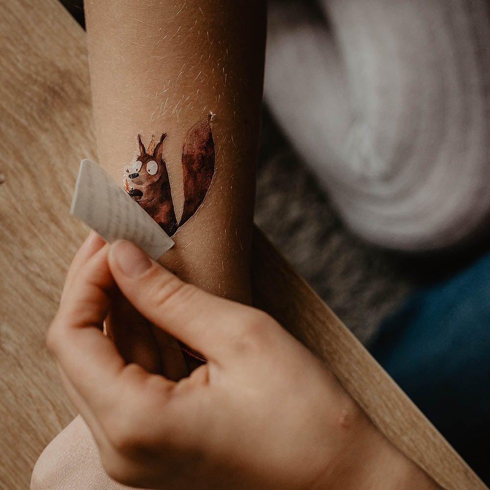Kind zieht ein Papier ab unter dem sich ein Eichhörnchen Tattoo auf seiner haut befindet