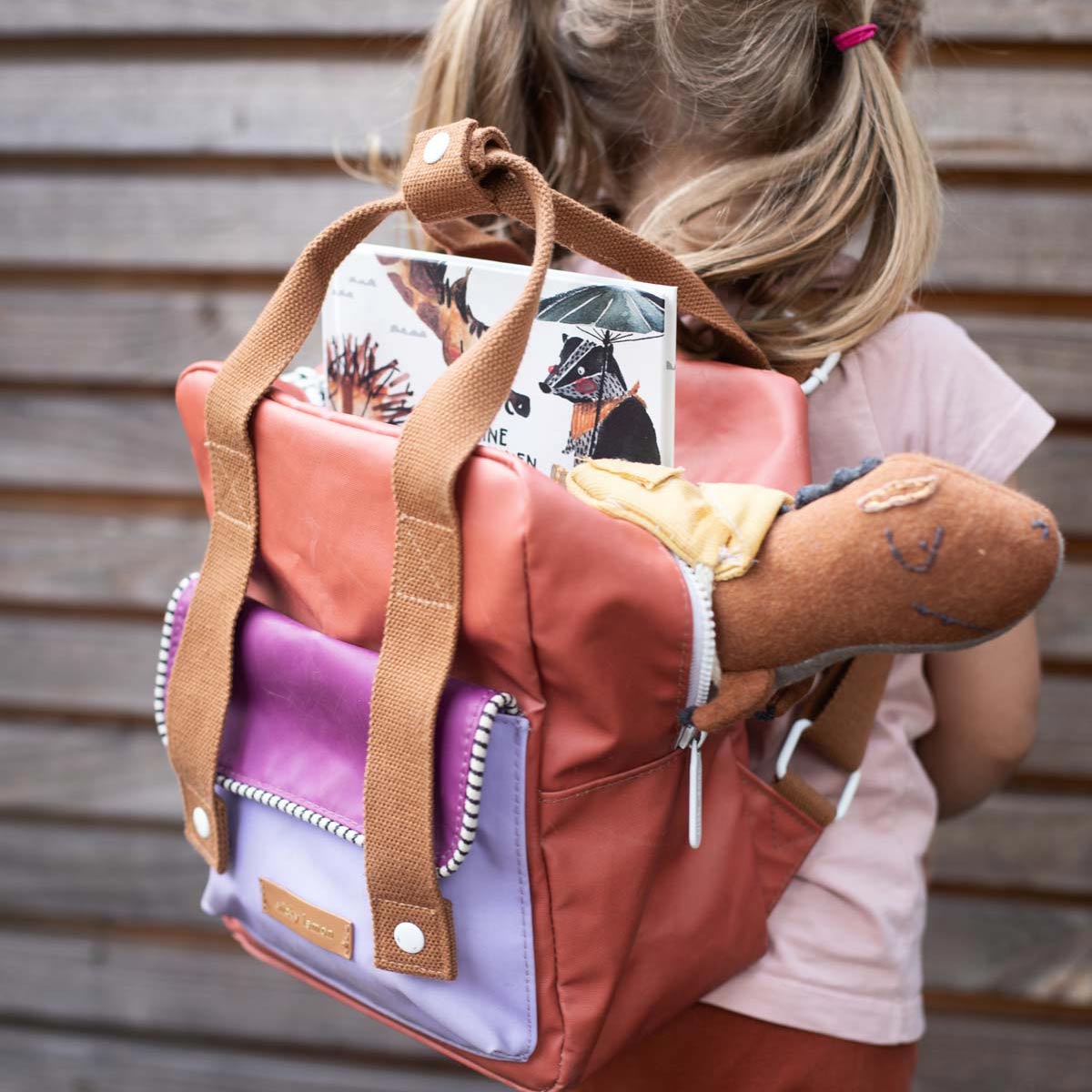 Kind mit Kindergarten-Rucksack gefüllt mit dem Freundebuch und Stofftier- T-Rex von Halfbird