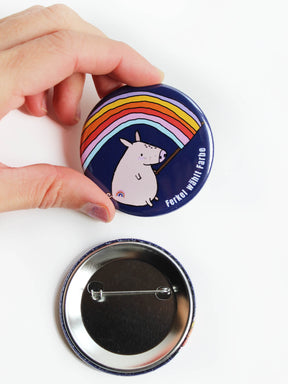Ansteckbutton mit sicherheitsnadel in dunkelblau mit Schweinchen, dass eine bunte regenbogenfahe hält und ein Regenbogen auf dem Po hat seitlich steht der Text Ferkel wählt Farbe