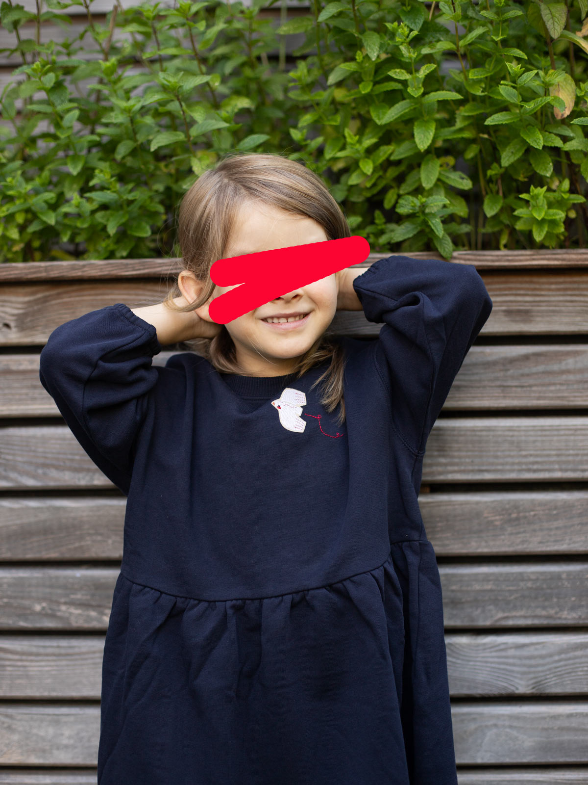 Kind mit dunkelblauem Kleid mit Friedenstauben-Aufnäher von Halfbird und roter, gestickter Fluglinie