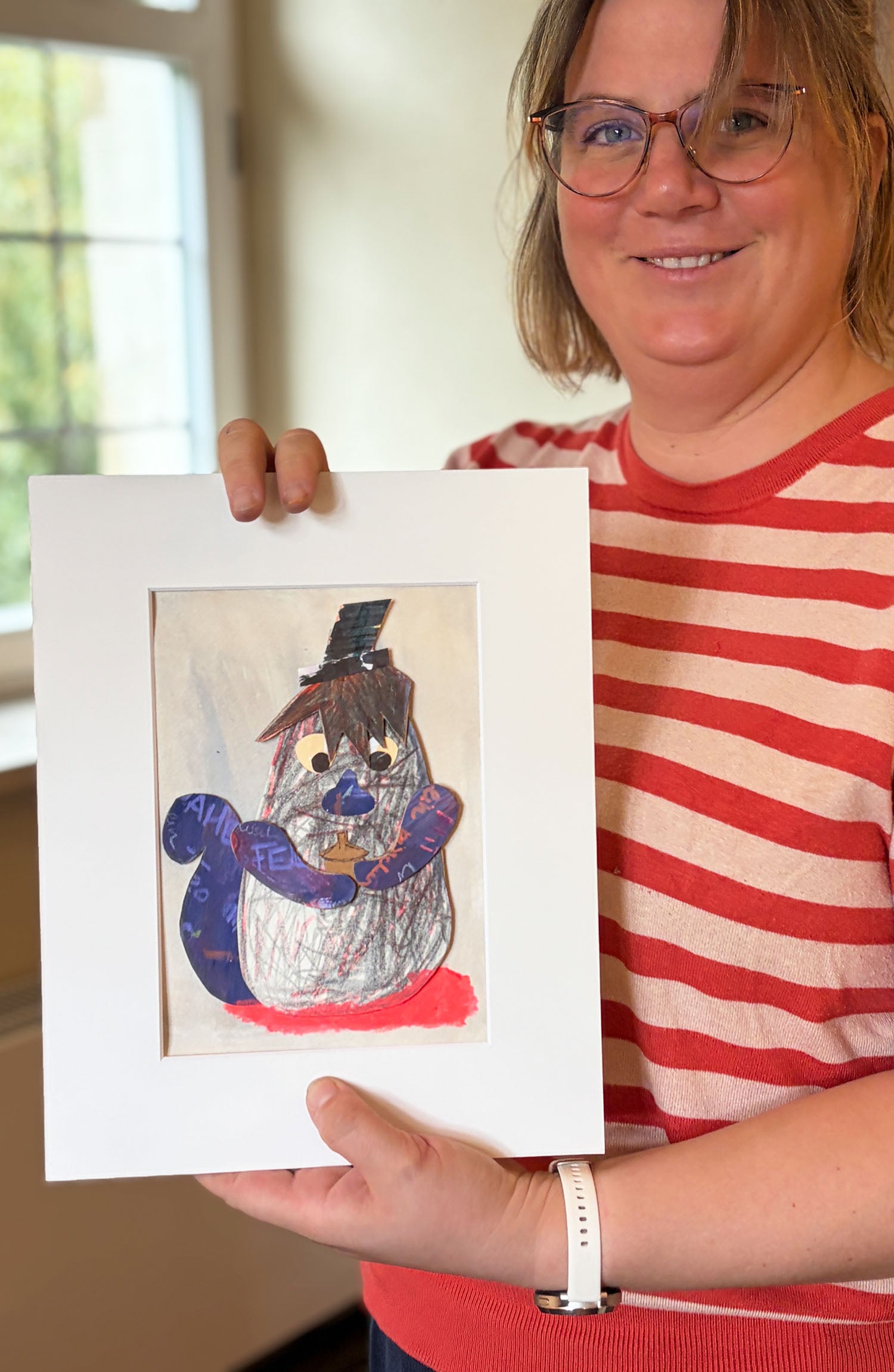 Eine Frau in rot weiß gestreiftem Oberteil hält ein Kunstwerk mit passepartout in den händen es zeigt ein Eichhörnchen aus papierresten