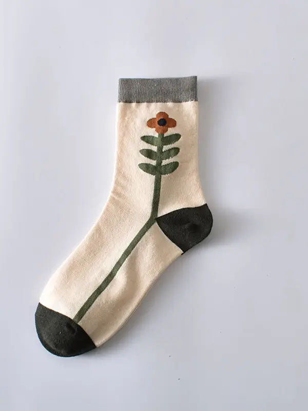 Flatlay von weißen Socken mit einer grün-orangenen Blume, die den Fuß entlang rankt und grauem Bündchen