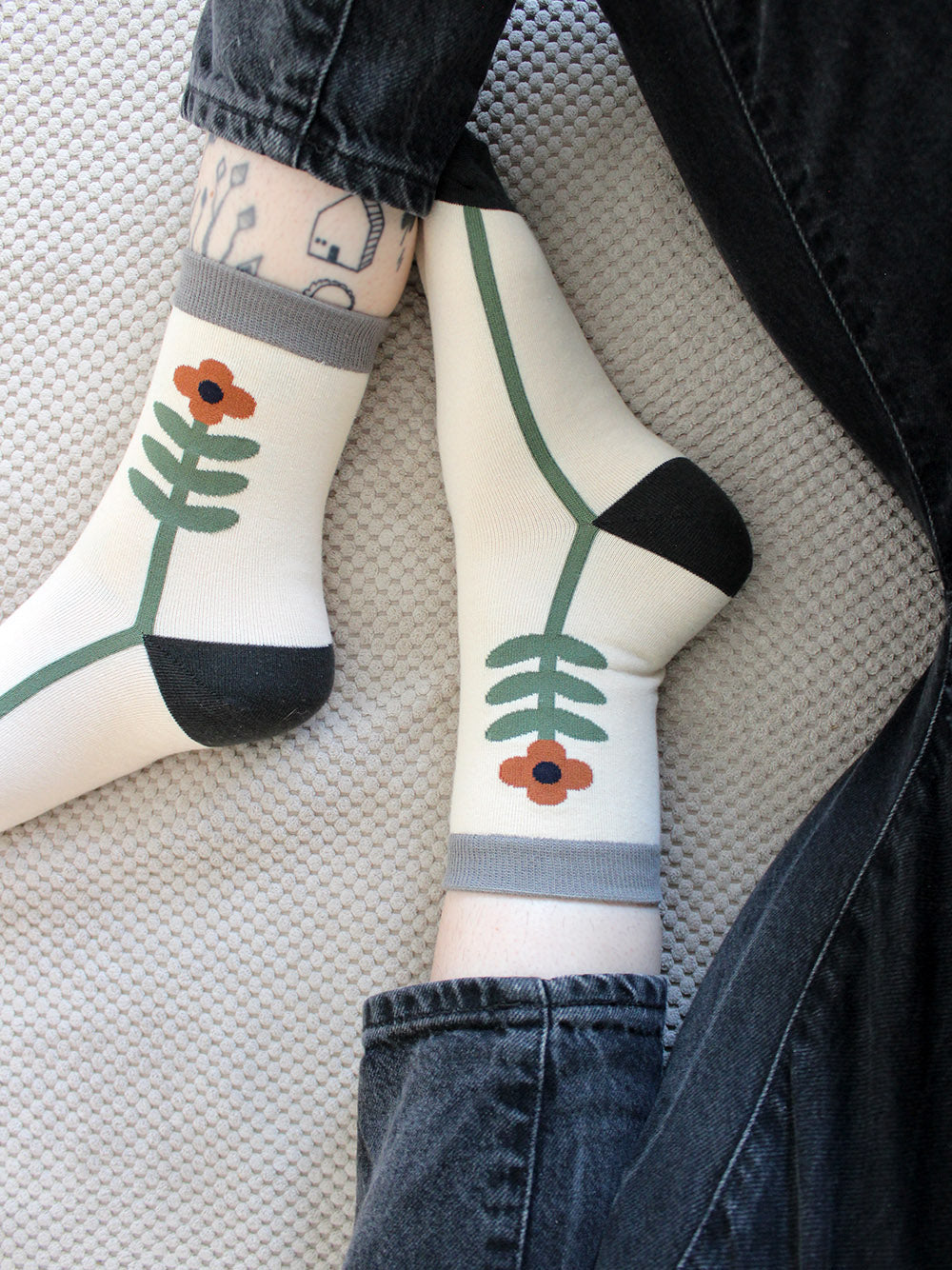 Tragebild von weißer Socke mit einer grün-orangenen Blume und grauem Bündchen