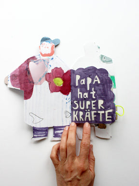 Aufgeschlagenes Superkräftebuch von Halfbird mit lila "Papa hat Superkräfte"-Seite
