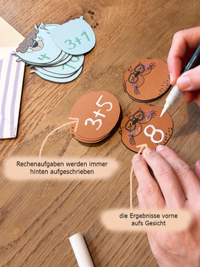 Hand malt mit einem weißen Acrylstift Rechenaufgaben und -ergebnisse auf die Stapelkarten von Halfbird im Otter-Design.