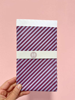 Hand mit Geschenktüte mit lila-blauem Streifenmuster von Halfbird