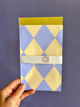 Hand mit Geschenktüte mit gelb-blauem Rautenmuster von Halfbird