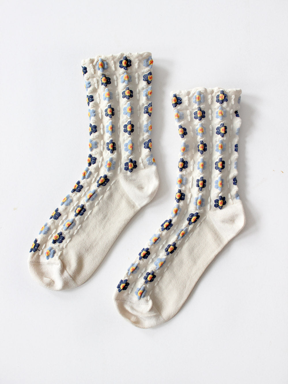 Flatlay von Cremefarbenen Socken mit Stickerei Anmutung und hellblauen und dunkelblauen Blumen mit gelb/roten Blütenstempeln