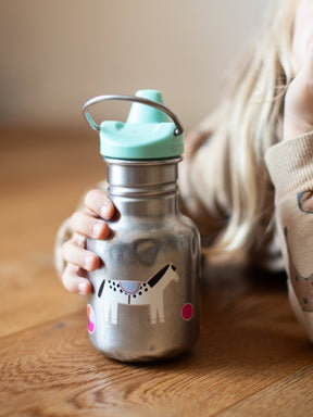 Kind sitzt am Tisch und hält eine edelstahl trinkflasche von klean kanteen in der hand, darauf kleben spülmaschinenfeste sticker von halfbird, ein pferd und bälle