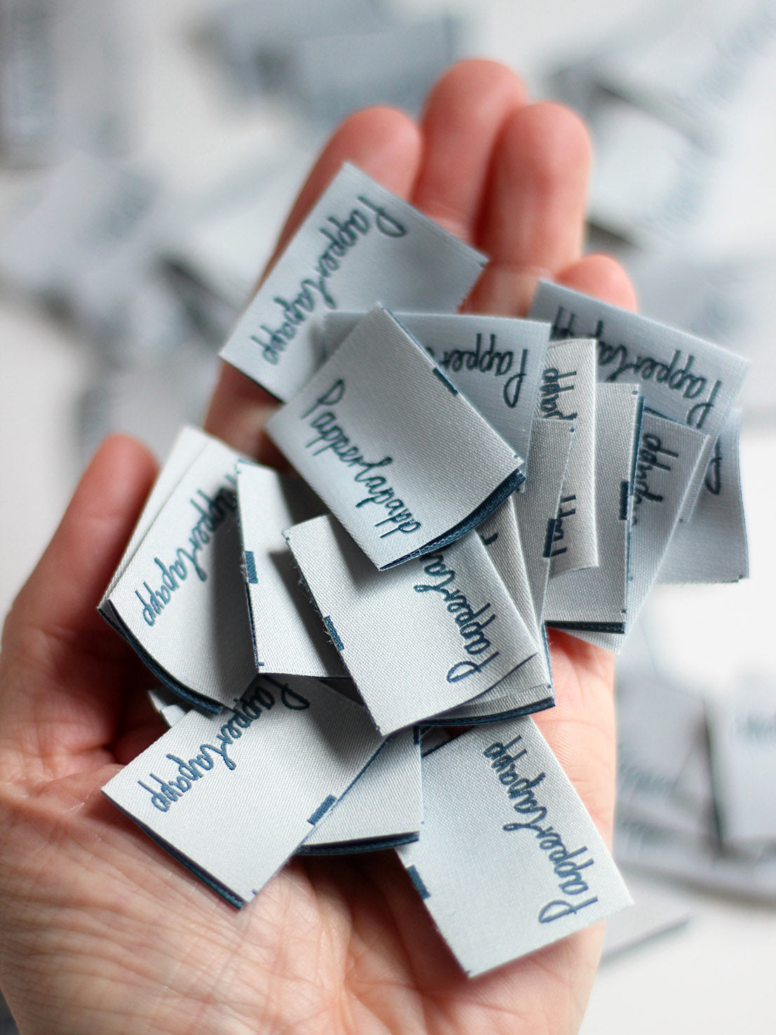 viele Etiketten in der Hand. Schriftzug Papperlapapp in grau und petrol